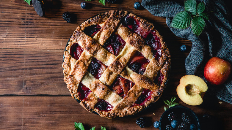 overhead view of a lattice-crust fruit pie on a wooden table beside various fruits