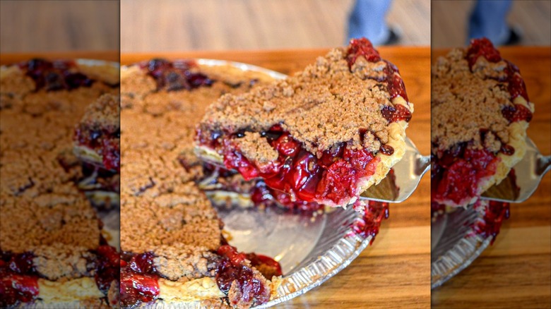 Metal spatula lifting slice of cherry crumble pie out of pan