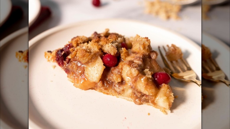 Slice of cranberry apple pecan pie on white plate