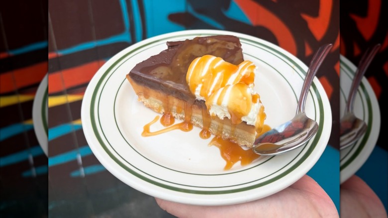 Close-up of hand holding white plate with millionaire shortbread pie and caramel drizzle