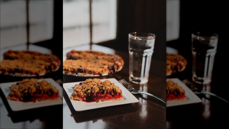Pie of fruit crumble pie on white plate, whole pie and glass of water in background