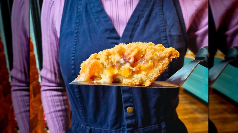 Piece of peach frangipane pie on spatula, person wearing blue and purple behind
