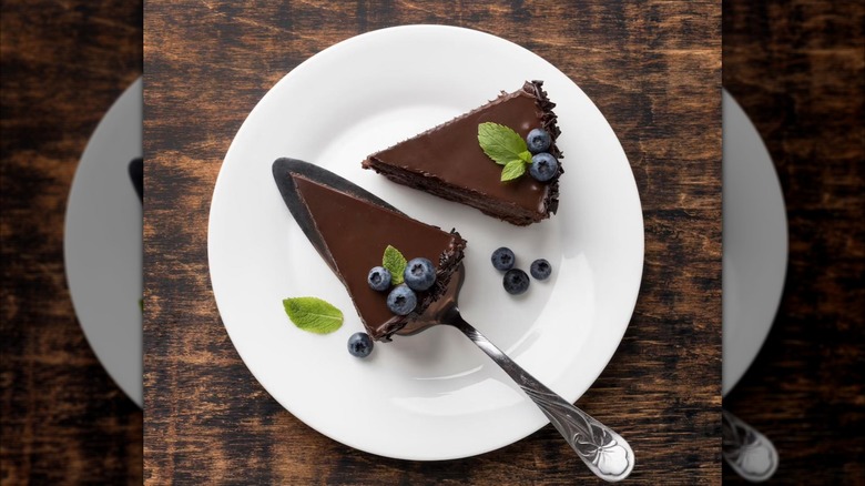 Top-down shot of two pieces of chocolate pie garnished with blueberries and mint on white plate