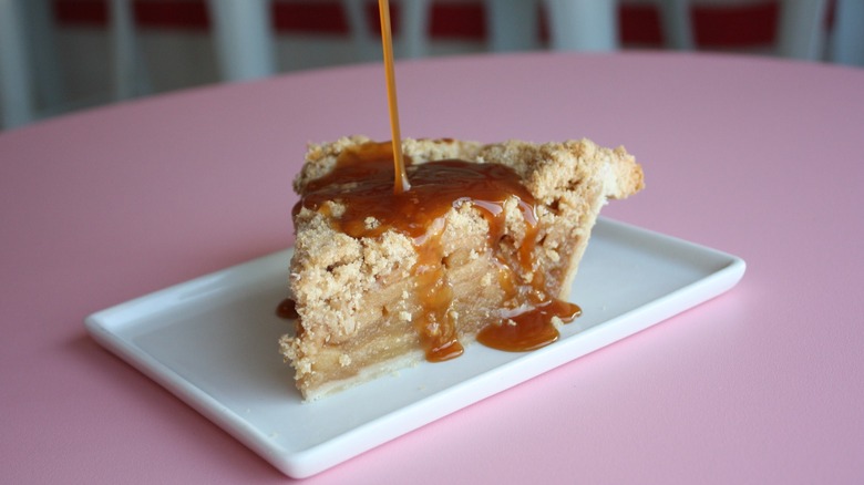 Close-up of apple crumble pie with caramel drizzle on white rectangular plate