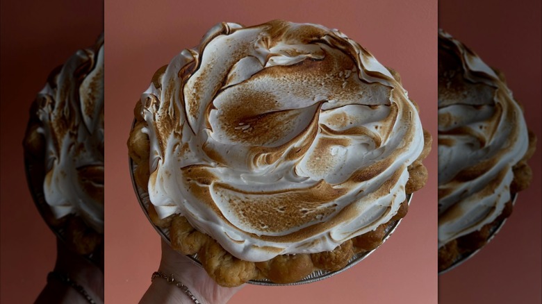 Hand holding pie with toasted meringue topping on pink background