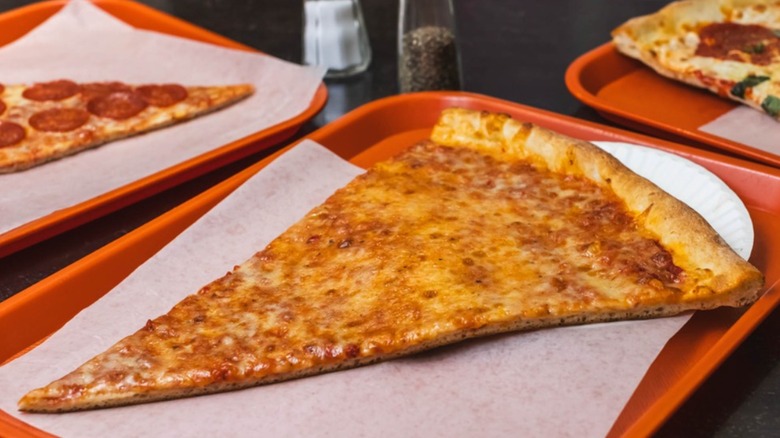 Large slice of cheese pizza on butcher paper and a paper plate on a red tray