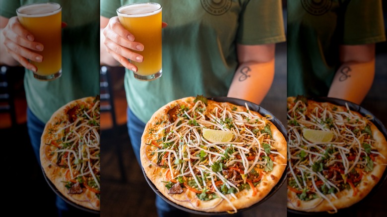 Curry pizza with bean sprouts, cheese, and lime wedge held by person with beer