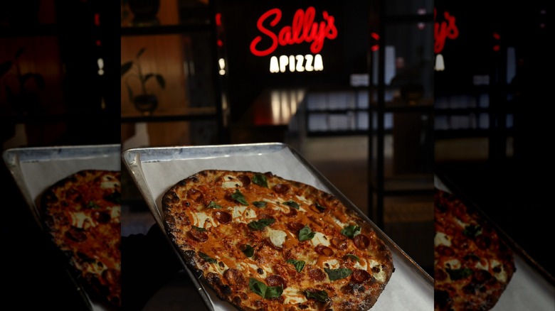 Round apizza on rectangular tray in front of neon Sally's sign