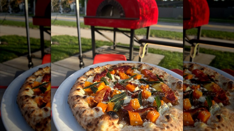 Pizza on a tray outside with oven in background