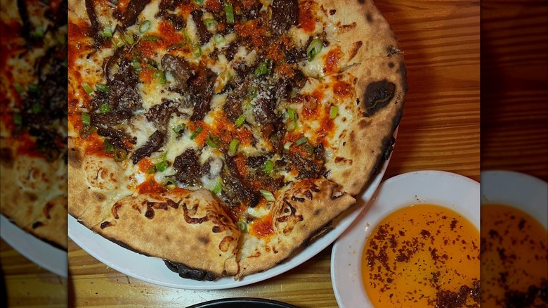 Pizza and bowl of dipping oil on wood-grain table