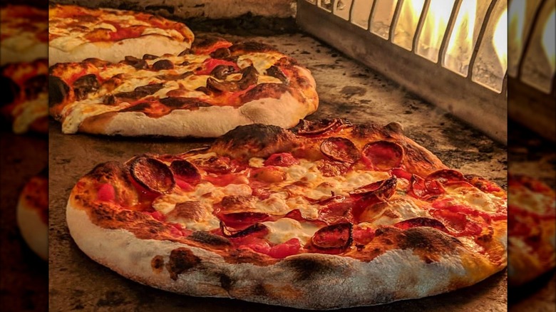 Three pizzas in an oven in front of the fire
