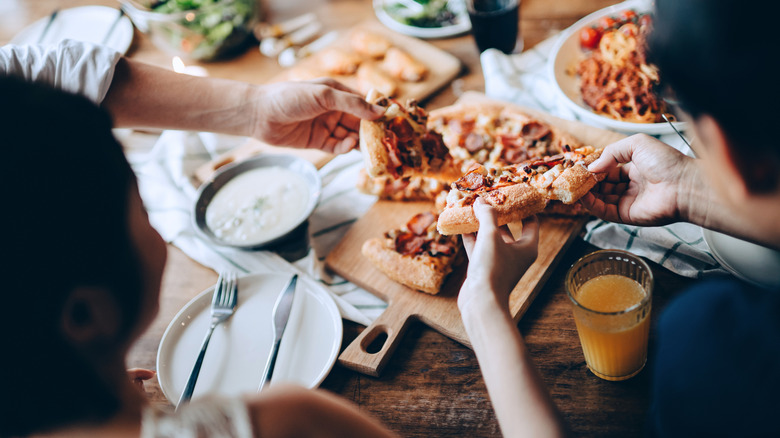 Groups of people sitting around a table eating pizza