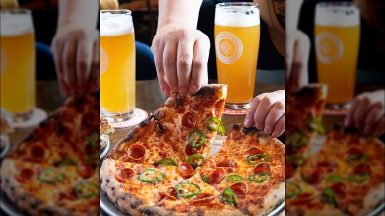 Hands picking up a slice from a pepperoni and jalapeno pizza