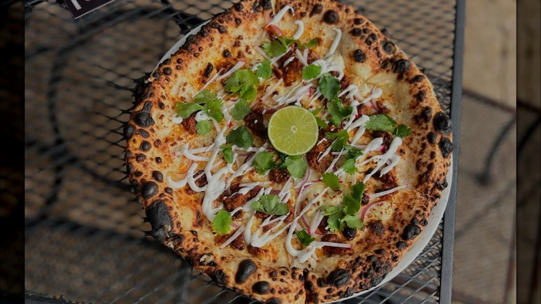 Wood-fired pizza with al pastor, cilantro, and a lime slice on metal table
