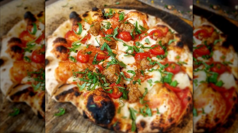 Wood-fired pizza on wooden peel with cheese, meatballs, and tomatoes