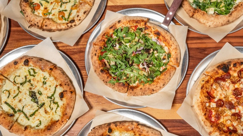 Wooden table with assortment of pizzas on silver trays