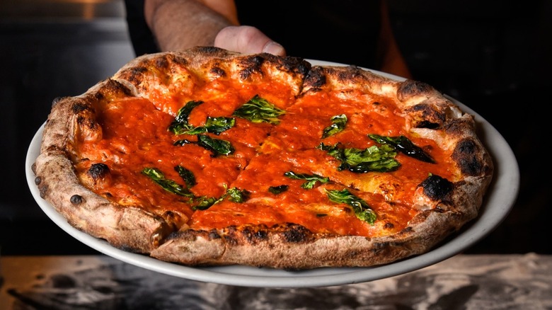 Hand holding saucy pizza on silver tray