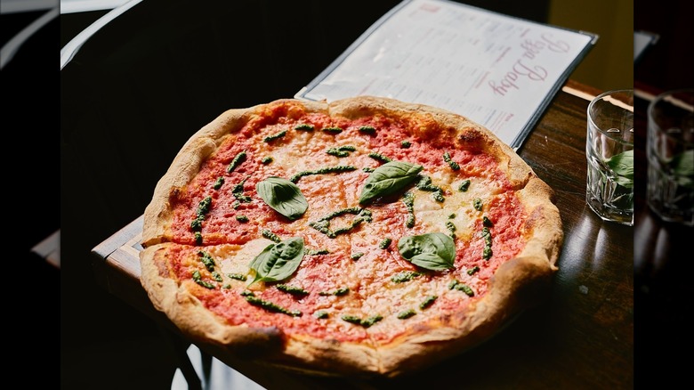 Pizza with basil leaves on a wooden table with Pizza Baby menu