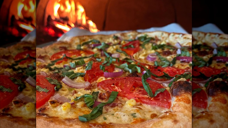 Wood-fired pizza with tomatoes and corn in front of a fire