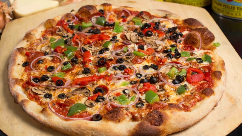 Pizza with peppers, black olives, and onions on a wooden board