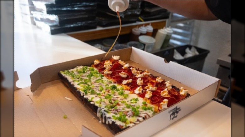 Sauce being drizzled on a half-and-half pizza in a box