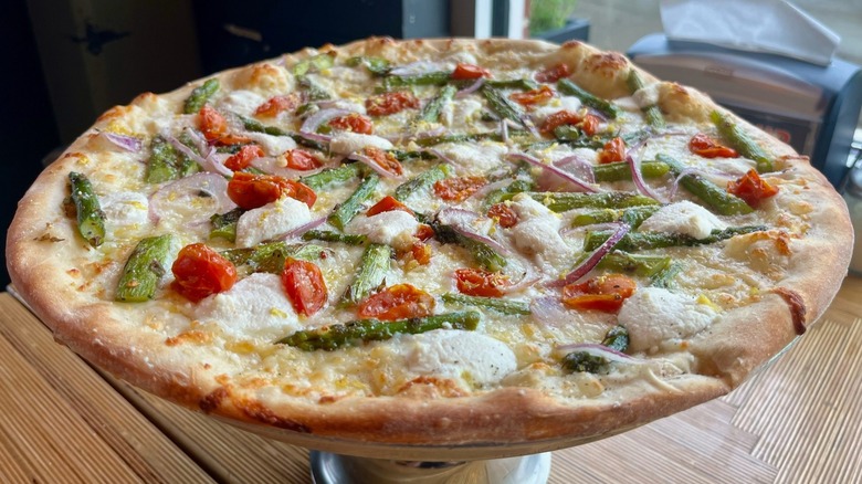 Pizza on stand with asparagus, tomato, onion, and mozzarella