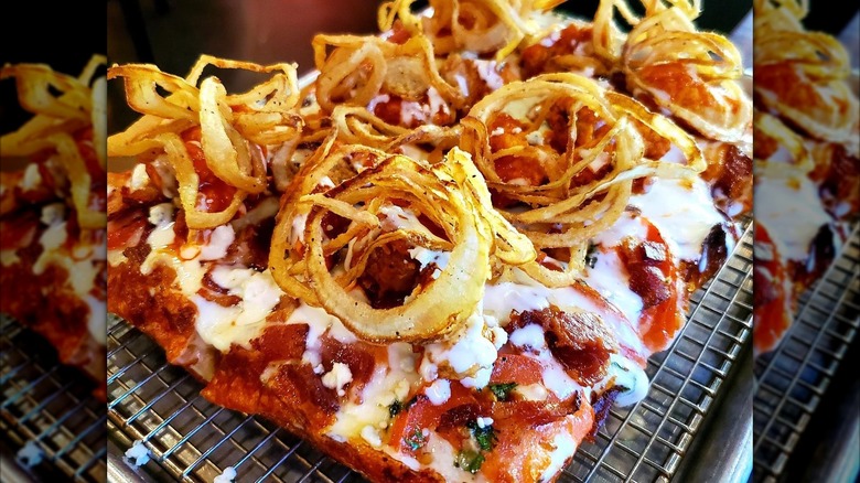 Deep-dish pizza with fried onion on metal tray