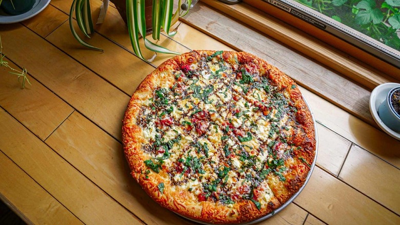 Goat cheese and tomato pizza on a windowsill with plants