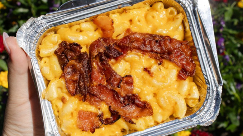 Hand holding bacon mac and cheese in aluminum tray