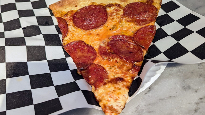 Slice of pepperoni pizza on checkered paper at Secret Pizza