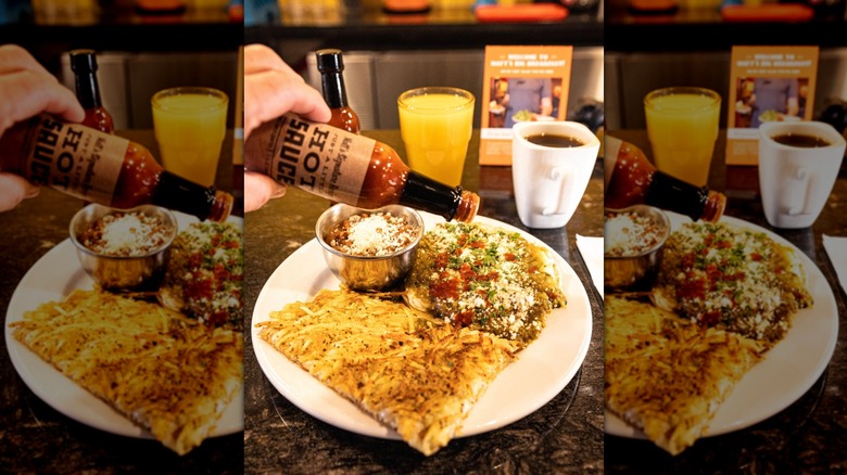 Hand pouring hot sauce onto breakfast plate with scramble and hash browns at Matt's Big Breakfast
