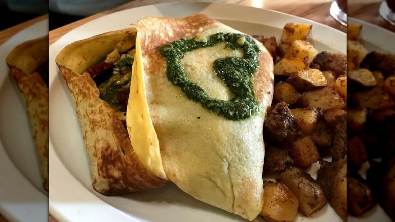 Breakfast potatoes next to egg with pesto heart on top on white plate at Foolish Craig's Cafe