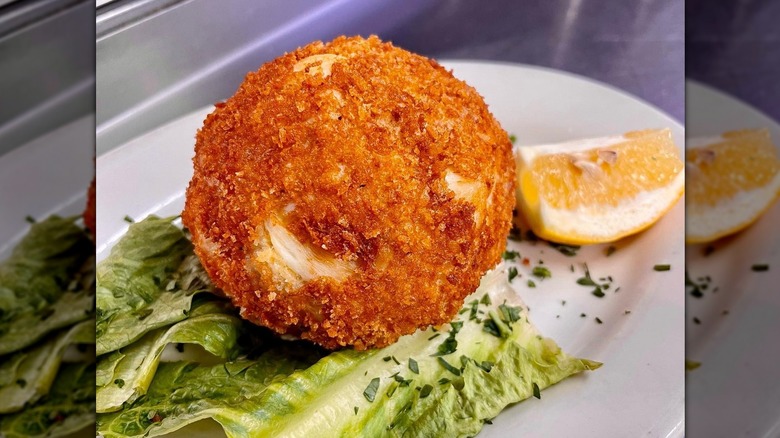 Crab cake on lettuce next to lemon wedge on white plate at Mrs. Robino's