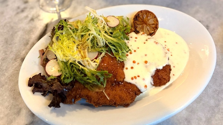 Gravy on fried meat topped with greens on white plate at The General Muir