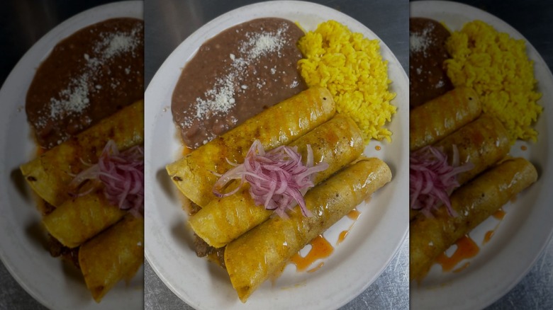White plate with rolled tortillas topped with red onions, next to yellow rice and beans at Jarocho, Kansas