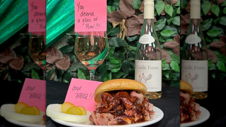Pulled meat sandwich on white plate with glass of white wine and bottle behind
