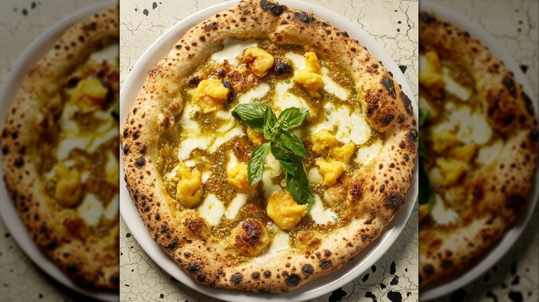 Close-up of pistachio pizza on white plate garnished with basil