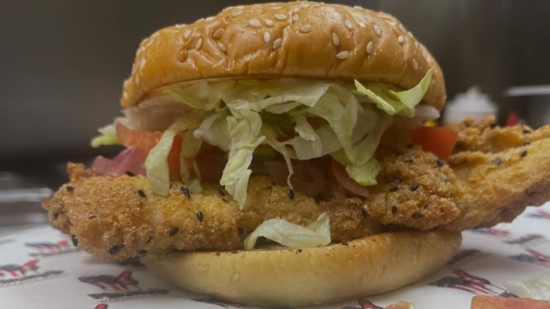 Close-up of haddock sandwich on seeded bun with lettuce, tomato