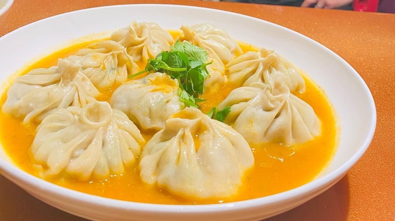 Chicken Jhol Momo in orange sauce in white bowl