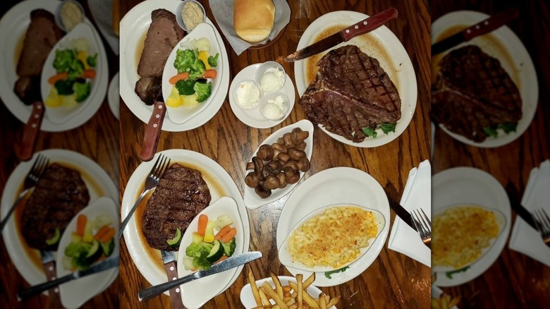 Top-down shot of steak dishes, mushrooms, mac and cheese, fries, steamed veggies on wood table