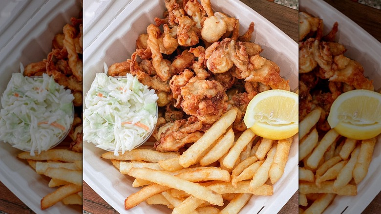 Top-down shot of styrofoam container with fried clams, coleslaw, fries, lemon wedges