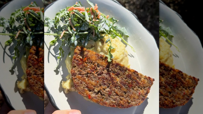 Top-down shot of meatloaf on mashed potatoes next to salad on white plate