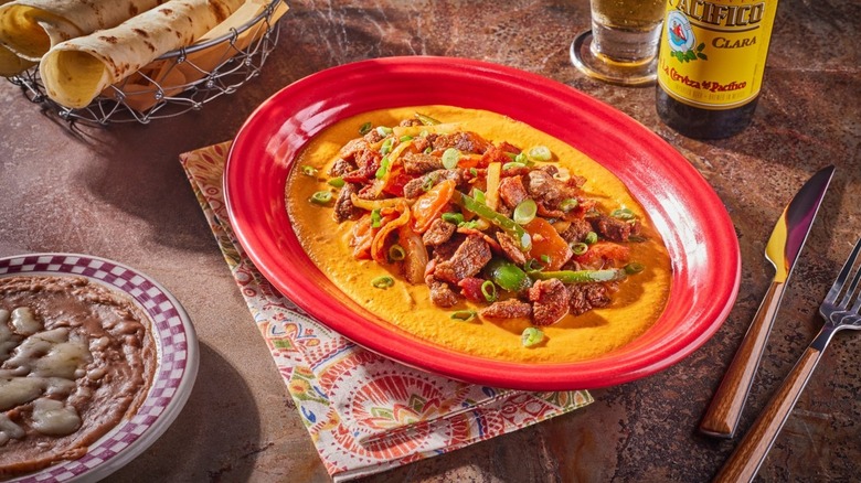 Puntas De Filete A La Norteña in red bowl on table, baked beans and tortillas beside