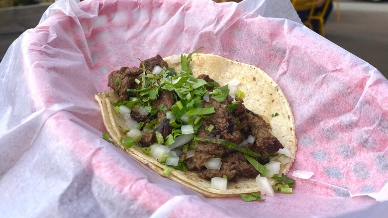 Steak taco with chopped onions and cilantro in basket