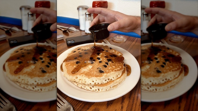 Hand pouring syrup onto pancake stack on white plate
