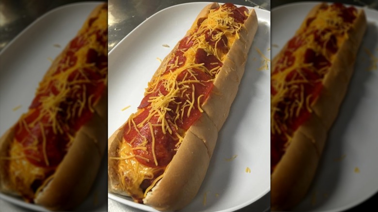 Big hot dog piled with cheese and pepperoni on white plate