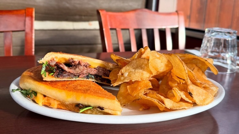 Short rib panini next to potato chips on white plate