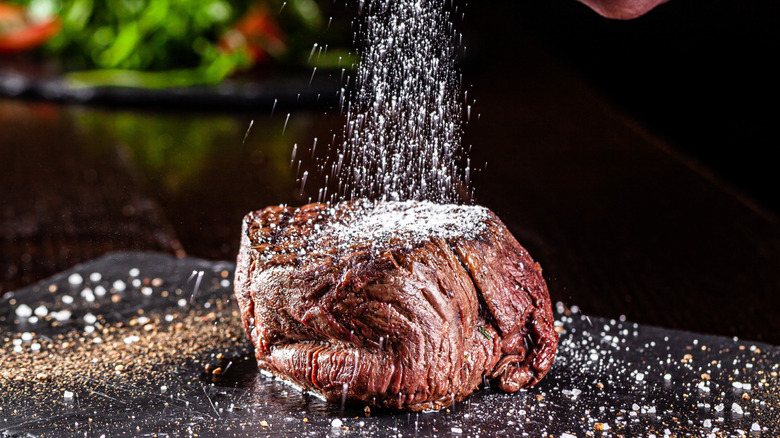 A filet steak being salted before cooking