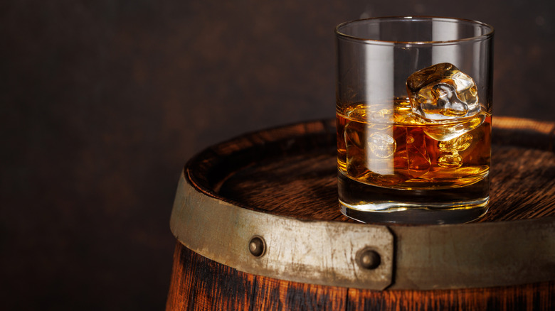 Glass of bourbon with ice, sitting on top of an oak barrel