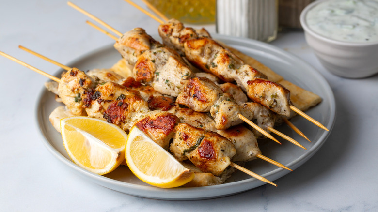 a plate of grilled chicken skewers with lemon wedges